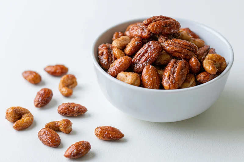 Candied spiced mixed nuts in a white ceramic bowl on a plain surface