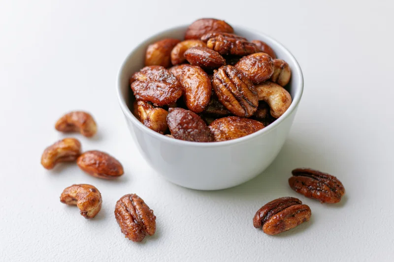 Candied spiced mixed nuts in a white ceramic bowl on a white surface