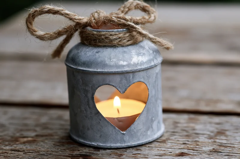 Lit candle in a zinc metal holder with heart cutout on wooden surface