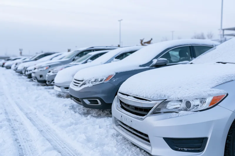 Snow-covered cars parked in a row in an outdoor lot during winter
