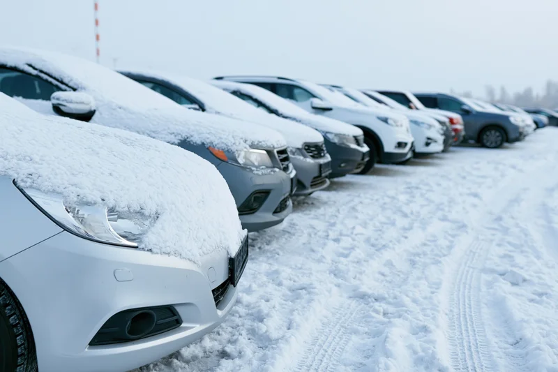Row of snow-covered cars parked in an outdoor lot during winter