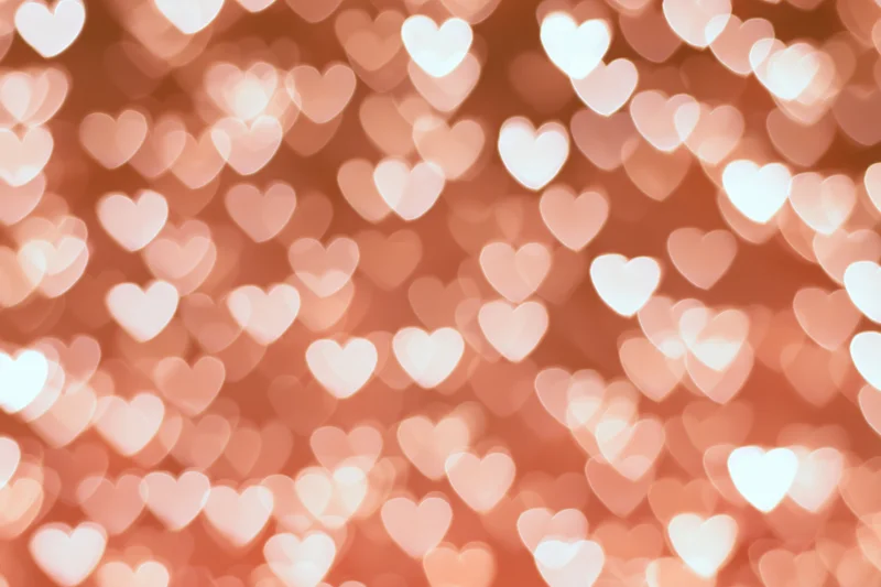Soft bokeh background of out-of-focus heart-shaped lights in warm pink tones