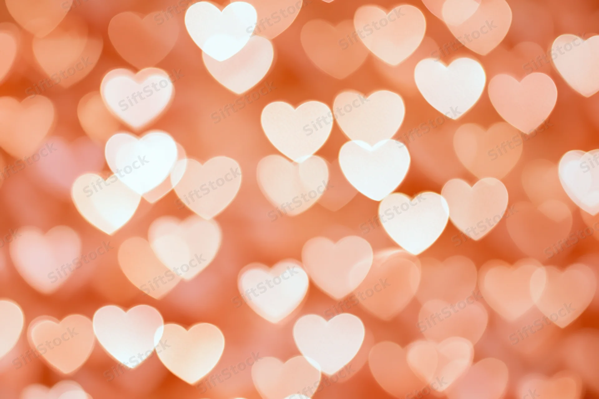 Soft bokeh background of glowing heart shapes in warm pink and peach tones