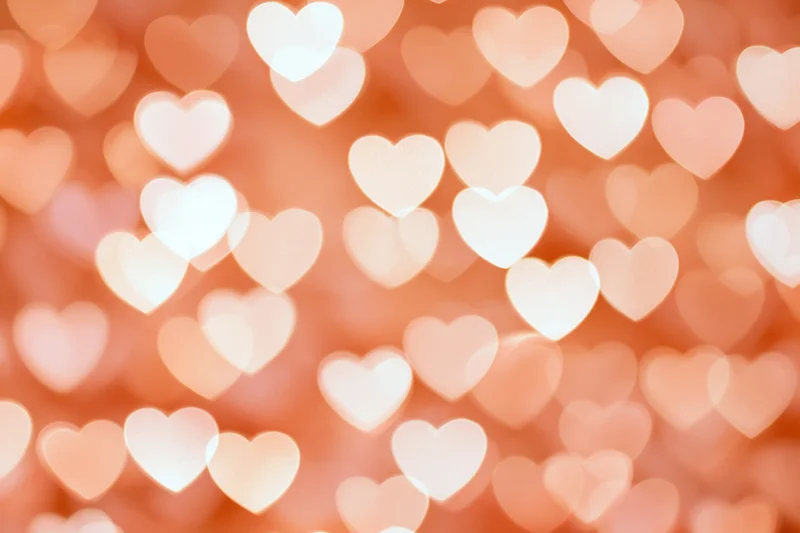 Soft bokeh background of glowing heart shapes in warm pink and peach tones