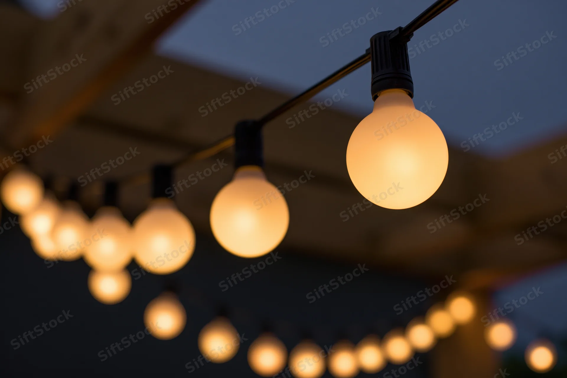 String of warm globe edison bulbs hanging outdoors at night under wooden ceiling