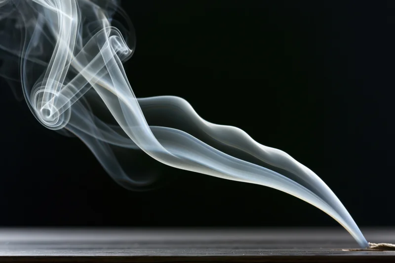 Thin white smoke curling upward from a wooden surface against a dark background
