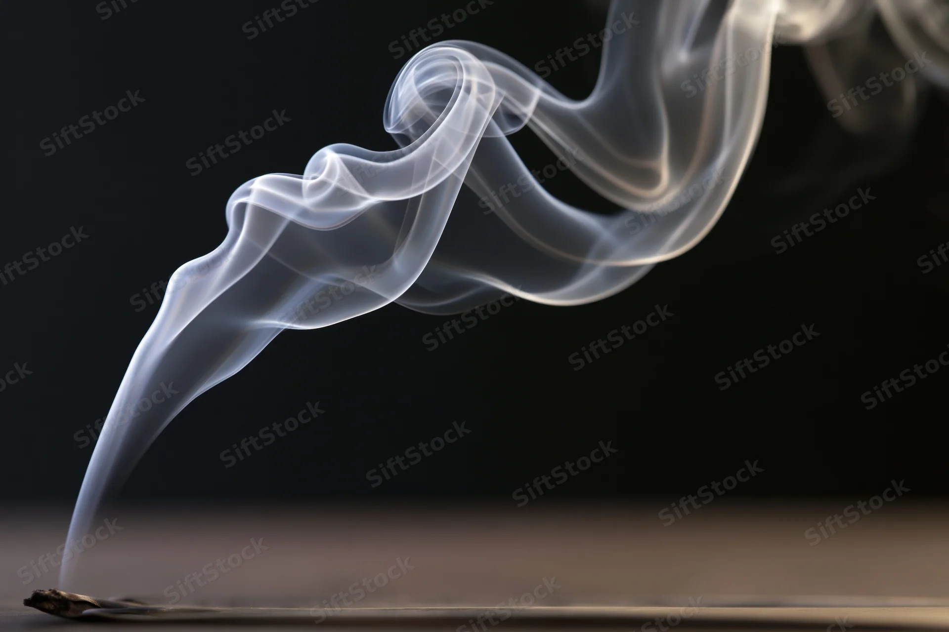 Thin white smoke curling upward from an incense stick on a dark surface
