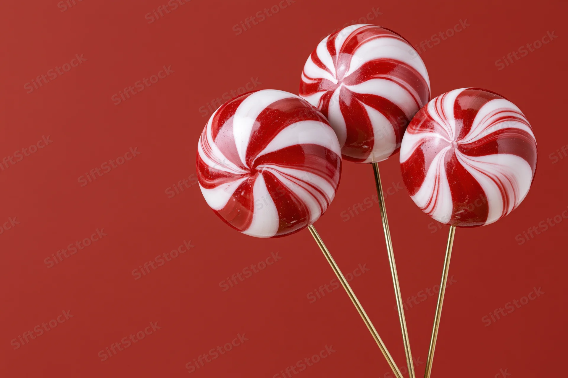 Three red and white swirled lollipops on gold sticks against a red background