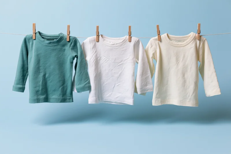 Three baby long-sleeve tops hanging on a clothesline against a light blue background