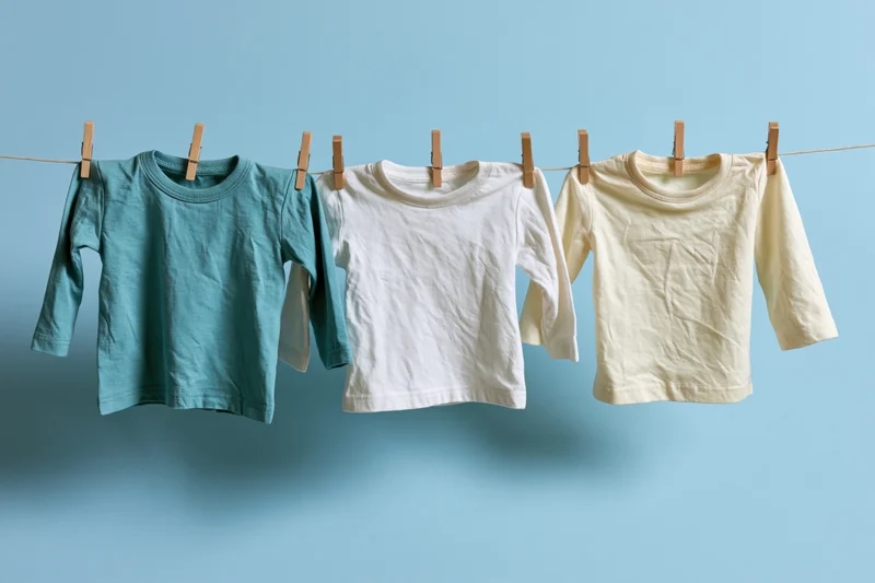 Three baby long-sleeve tops hanging on a clothesline against a blue background