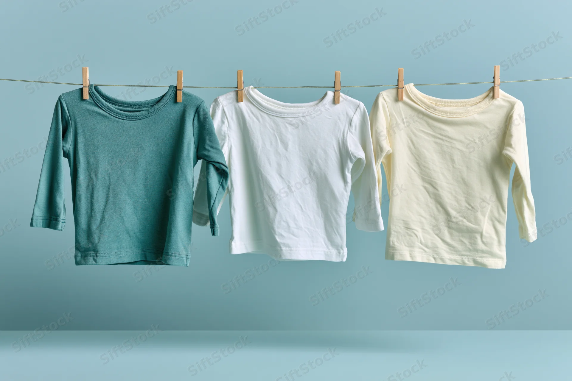 Three baby long-sleeve tops hanging on a clothesline against a light blue background