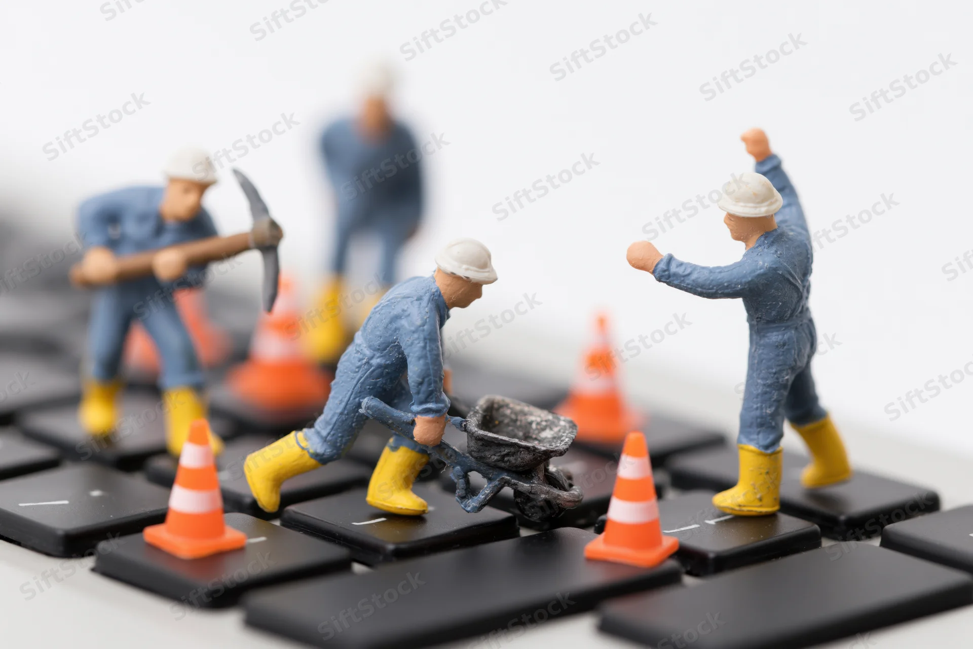 Miniature construction workers on a computer keyboard with safety cones and tools