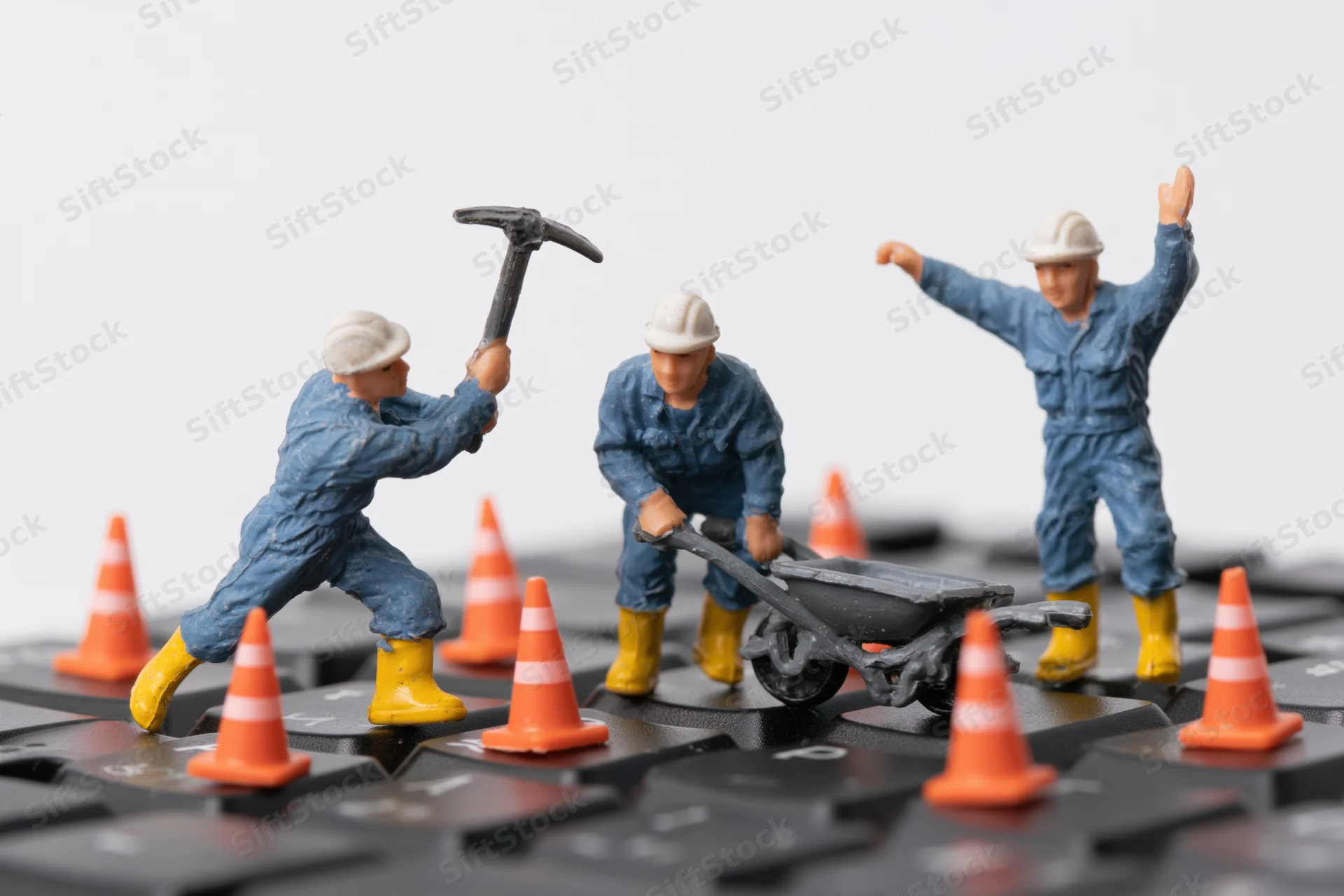 Miniature construction workers with tools and safety cones on a computer keyboard