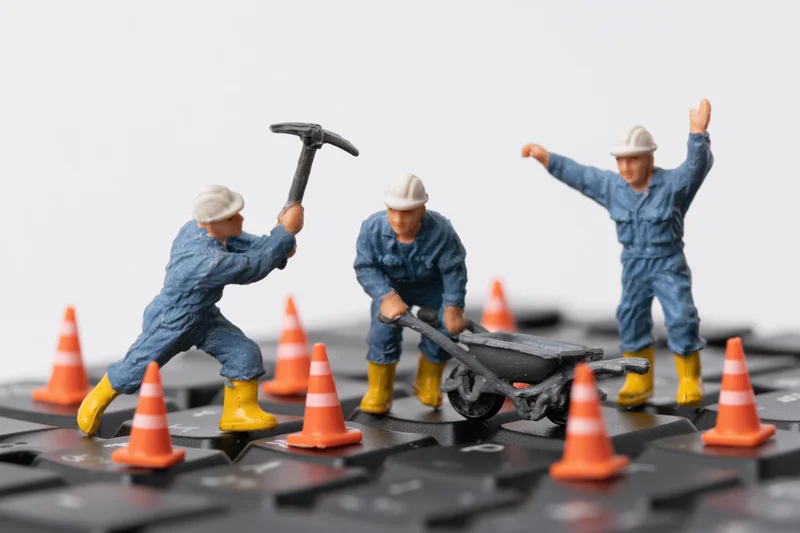 Miniature construction workers with tools and safety cones on a computer keyboard