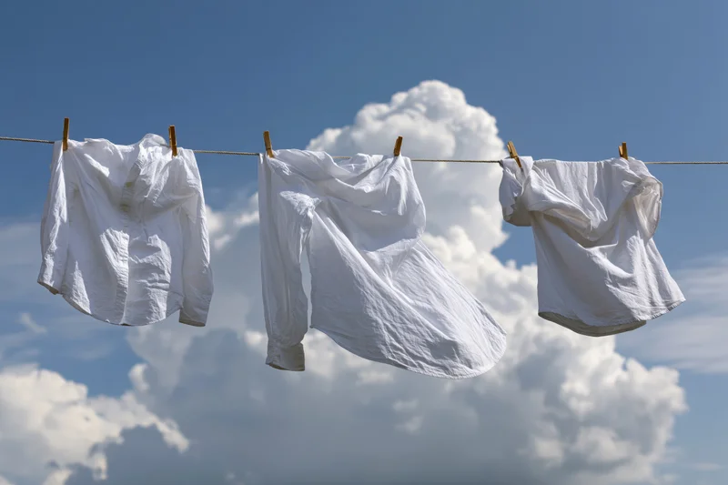 White cotton shirts drying on a clothesline against a blue sky with clouds
