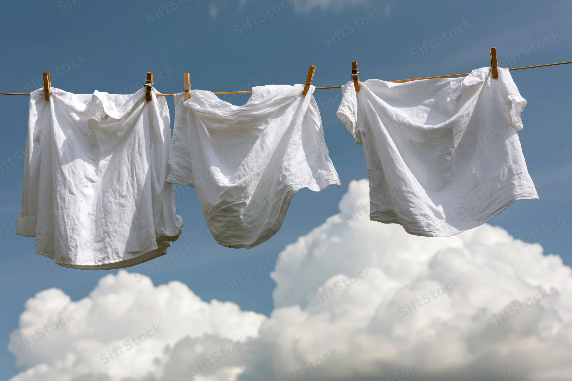 White cotton shirts hanging on a clothesline against a blue sky with clouds