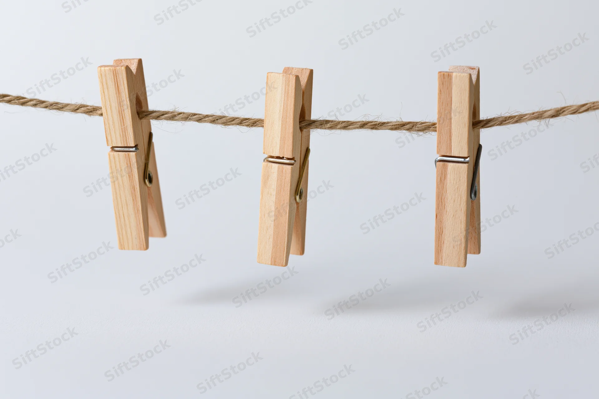 Three wooden clothespins clipped evenly along a natural rope against a white background