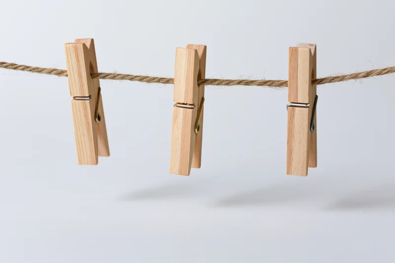 Three wooden clothespins clipped evenly along a natural rope against a white background