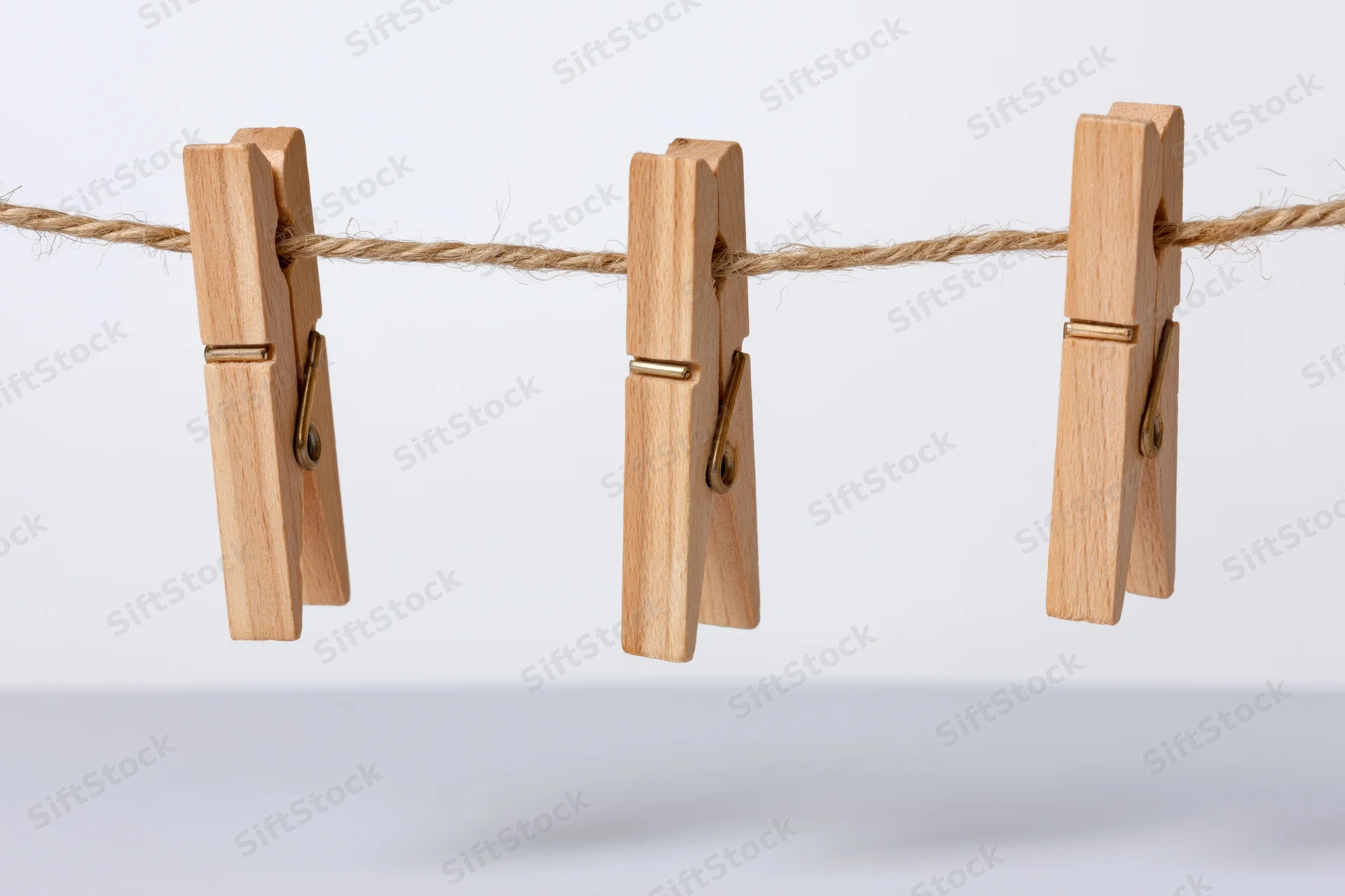 Three wooden clothespins clipped evenly along a natural twine clothesline against a plain white background