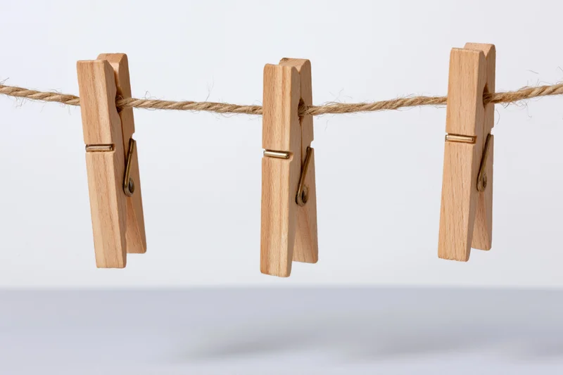 Three wooden clothespins clipped evenly along a natural twine clothesline against a plain white background