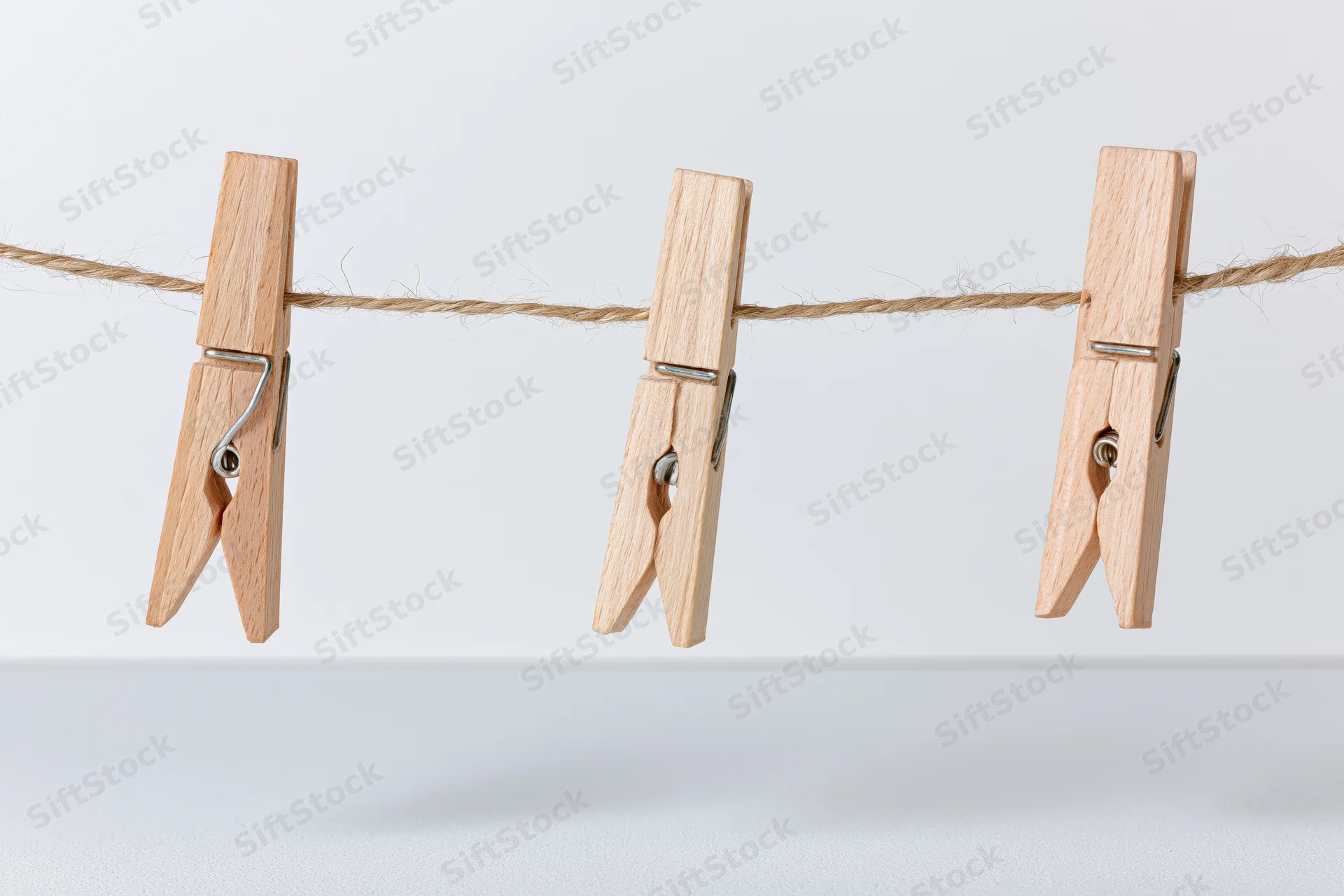Three wooden clothespins clipped evenly along a natural fiber rope against a white background