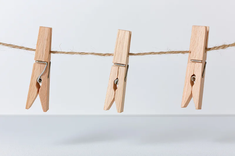 Three wooden clothespins clipped evenly along a natural fiber rope against a white background