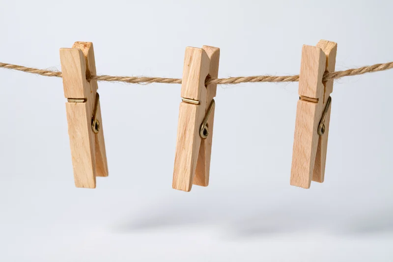 Three wooden clothespins clipped evenly along a natural twine clothesline against a white background