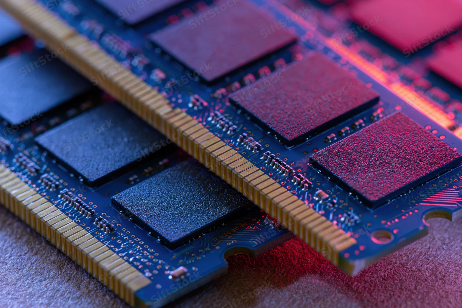 Two ddr ram sticks stacked on a circuit board surface under colorful lighting