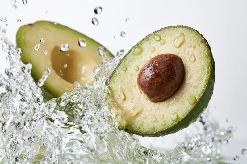 Two avocado halves midair surrounded by dynamic water splash against white background