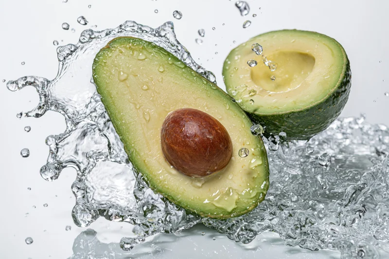 Two avocado halves midair surrounded by dynamic water splash on white background