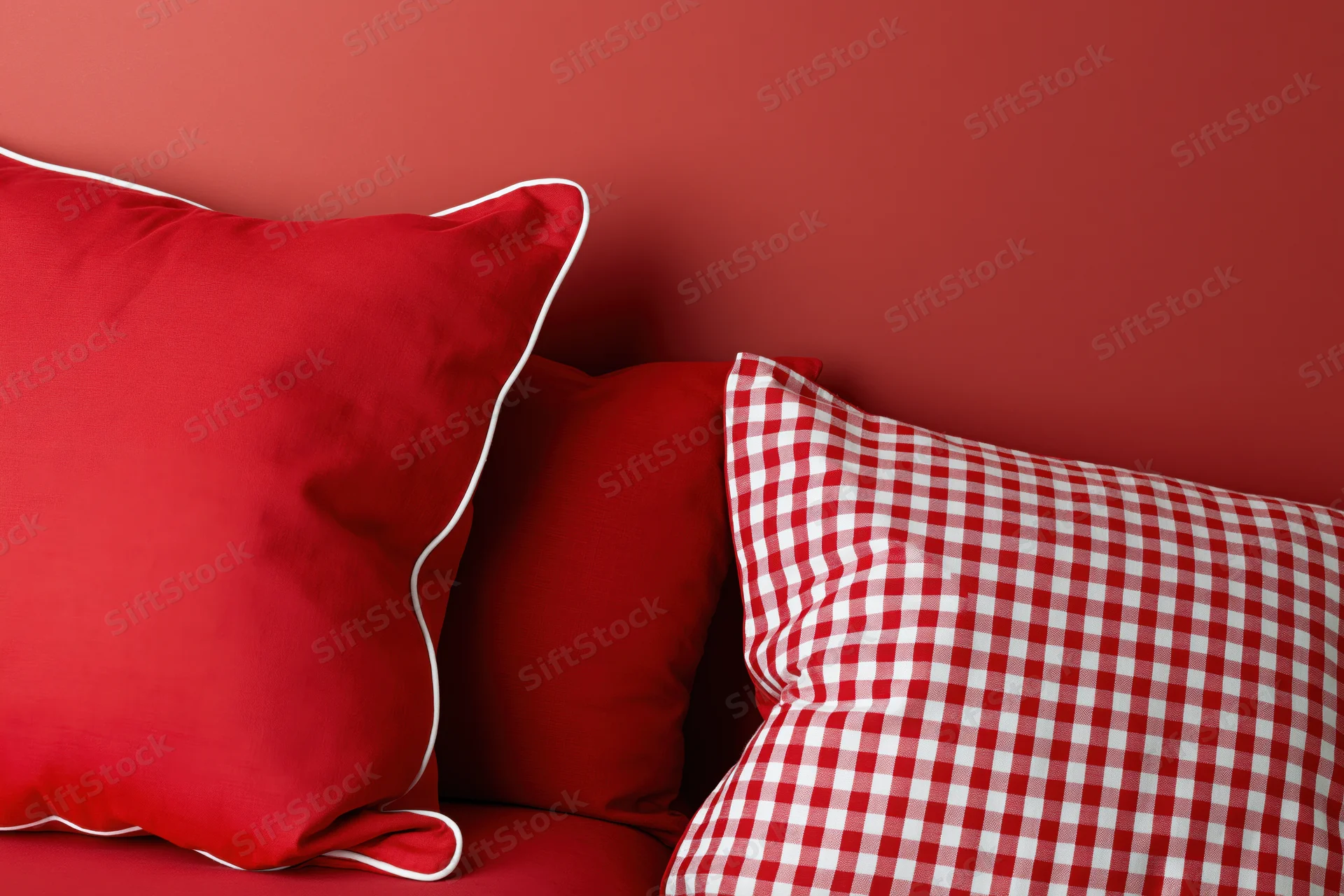 Red decorative pillows with white trim and checkered pattern resting against a red wall