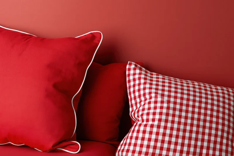 Red decorative pillows with white trim and checkered pattern resting against a red wall