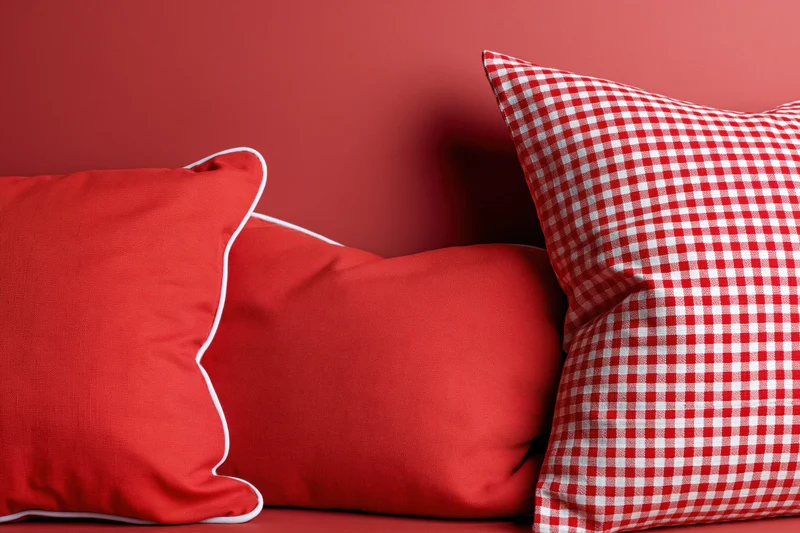 Three red decorative pillows arranged against a red wall, one with gingham pattern