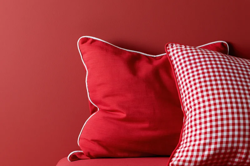 Two decorative pillows resting against a red wall with copyspace on the left
