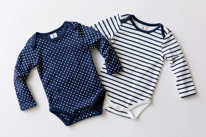Two infant longsleeve bodysuits with navy polka dot and white stripe patterns laid flat on white background