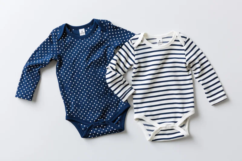 Two infant longsleeve bodysuits with navy polka dot and white stripe patterns laid flat on white background