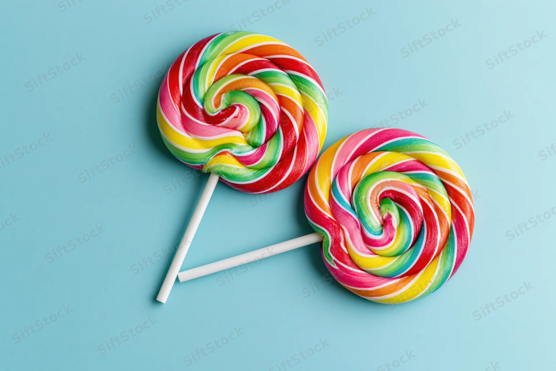 Two rainbow-swirl lollipops on a light blue background