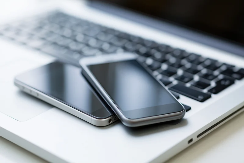 Two smartphones with black screens resting on a silver laptop keyboard