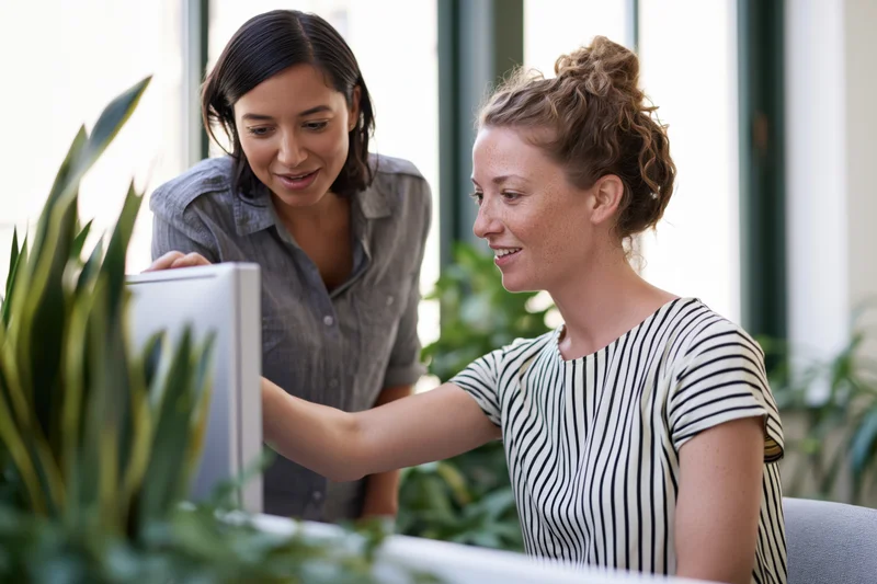 Two women collaborating at a desktop computer in a modern office