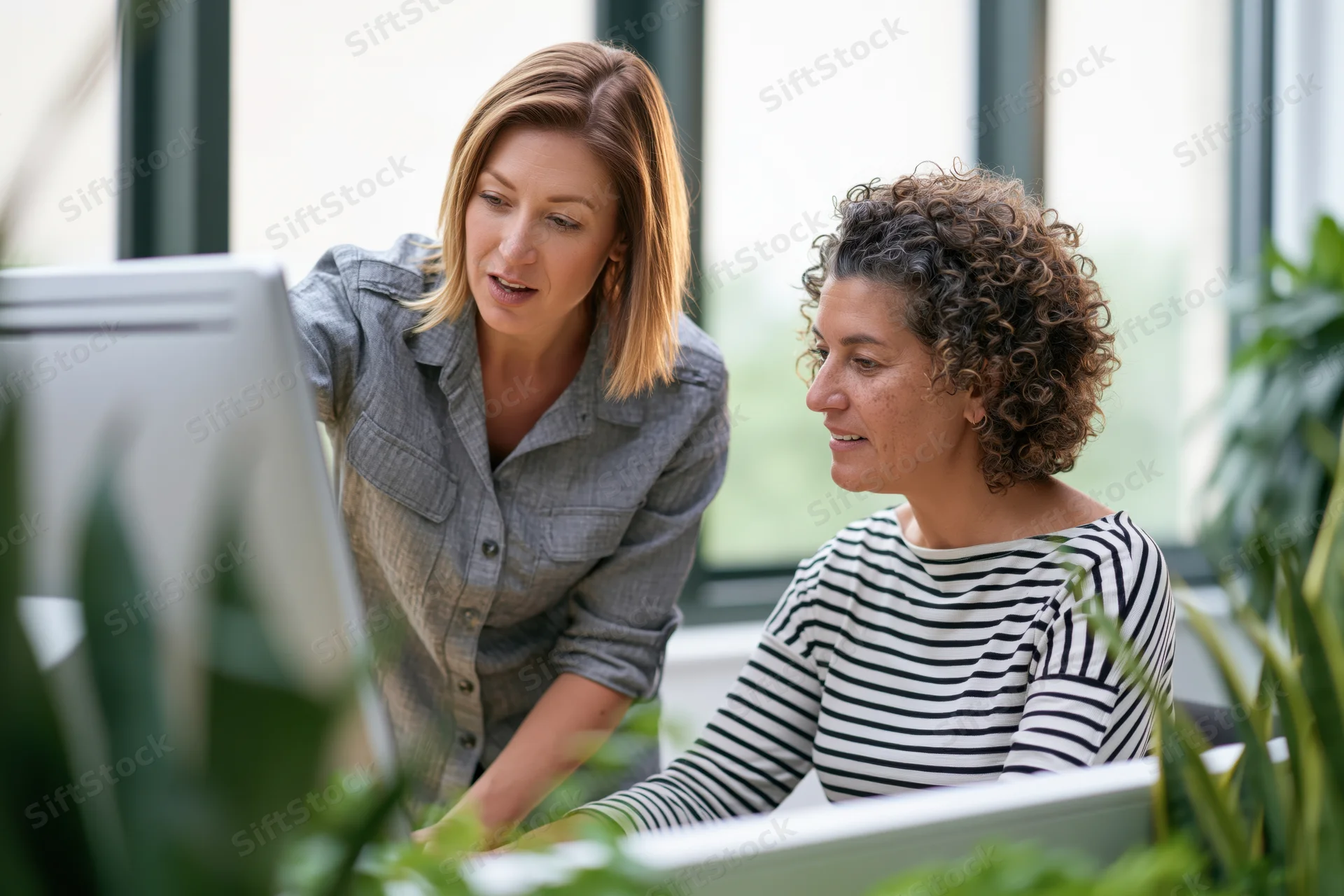Two women collaborating at a desktop computer in a modern office