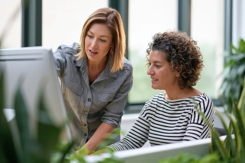 Two women collaborating at a desktop computer in a modern office