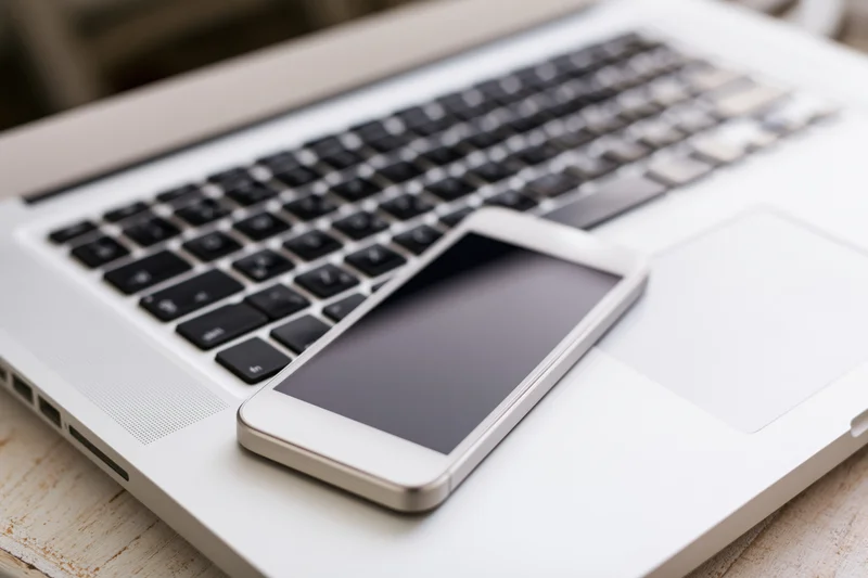 White smartphone with dark screen resting on open laptop keyboard on wooden desk