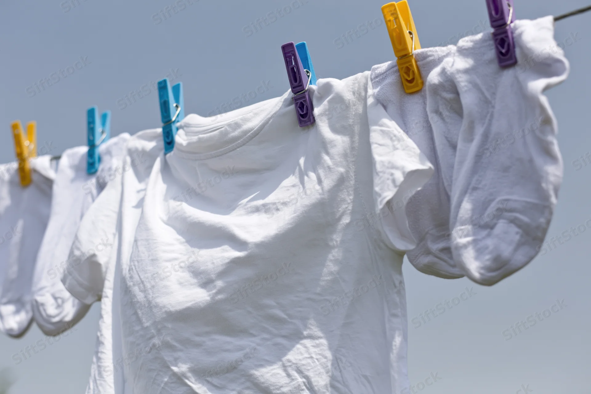 White t-shirt and socks clipped to a clothesline drying outdoors under a clear sky