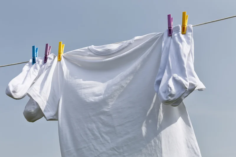 White t-shirt and socks hanging on a clothesline drying outdoors under a clear sky