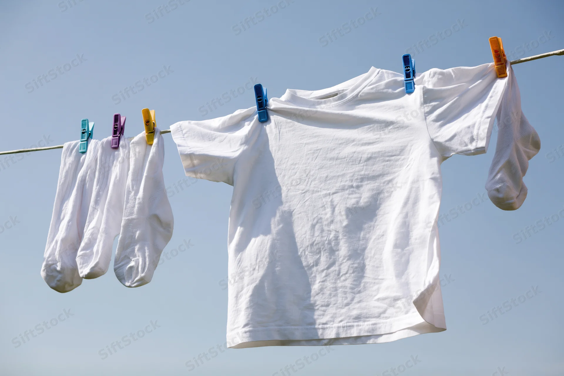 White t-shirt and socks hanging on a clothesline drying in the sun outdoors