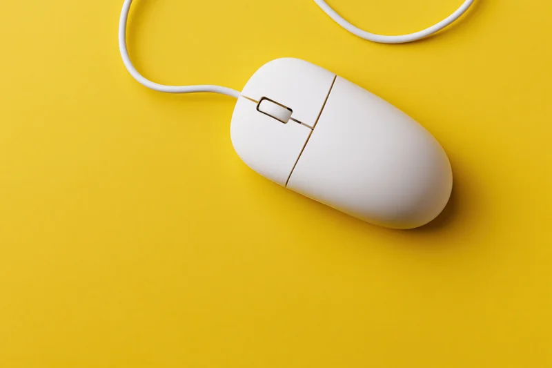White wired computer mouse on yellow surface with curved cable and copyspace