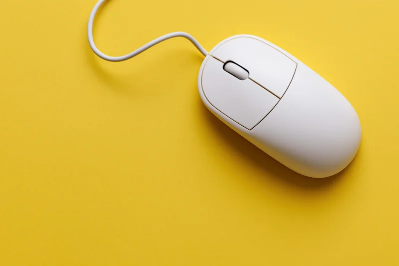 White wired computer mouse on yellow background with curved cable and copyspace