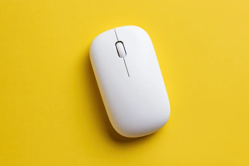 White wireless computer mouse centered on a flat yellow paper surface