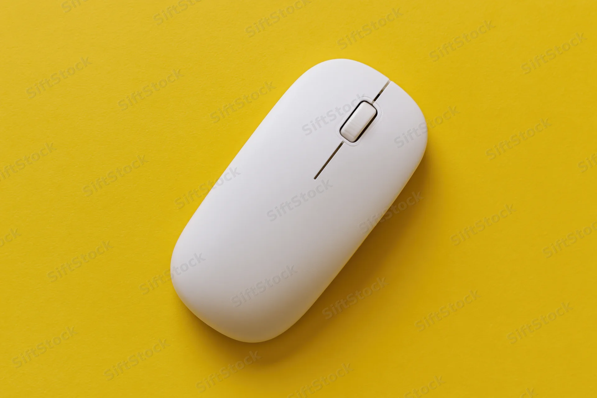White wireless computer mouse centered on a flat yellow paper surface