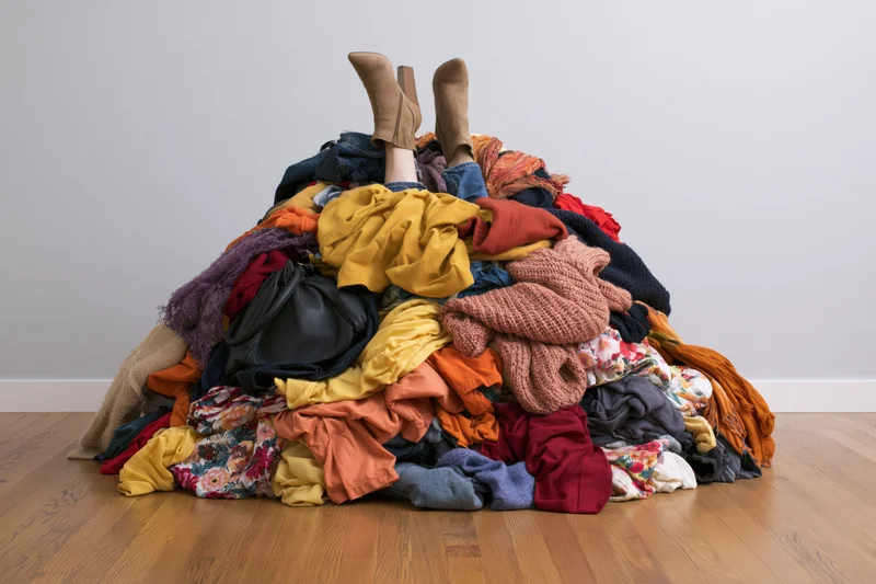 Woman’s legs sticking up from a large pile of colorful clothes on a wooden floor